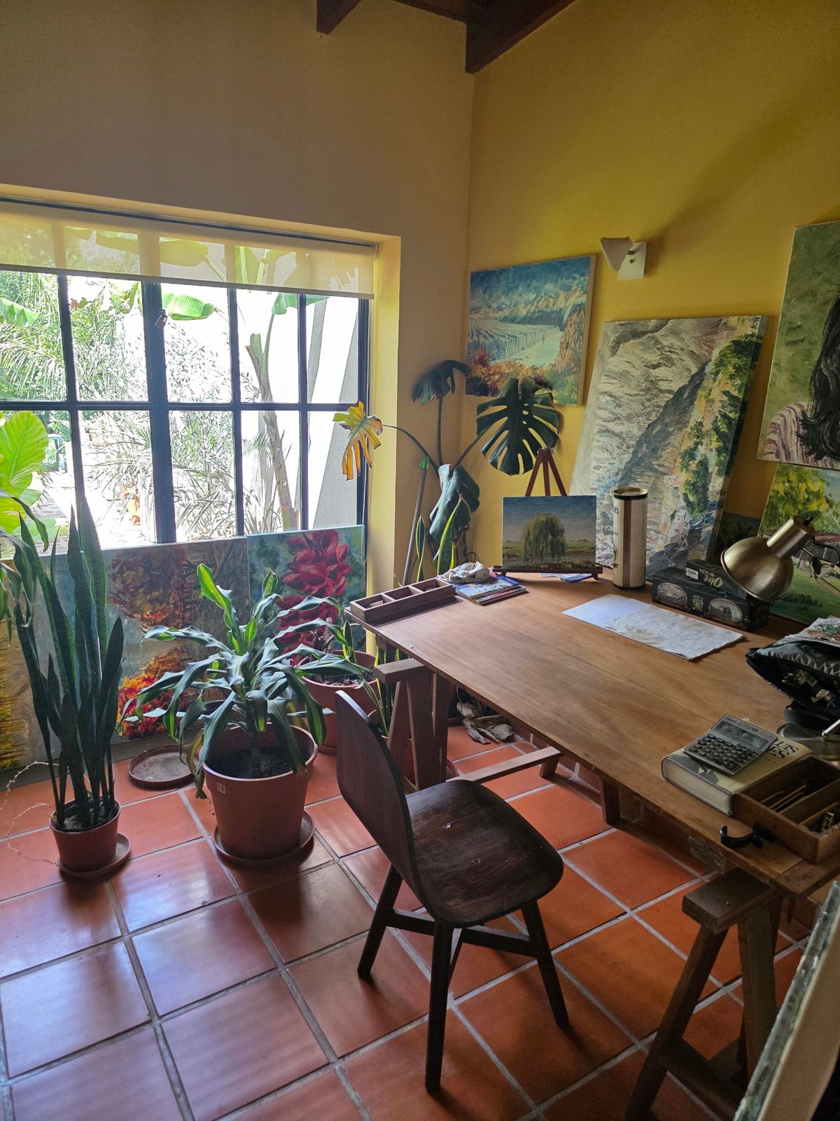 Mesa de trabajo del pintor junto a la ventana, con cuadros y plantas